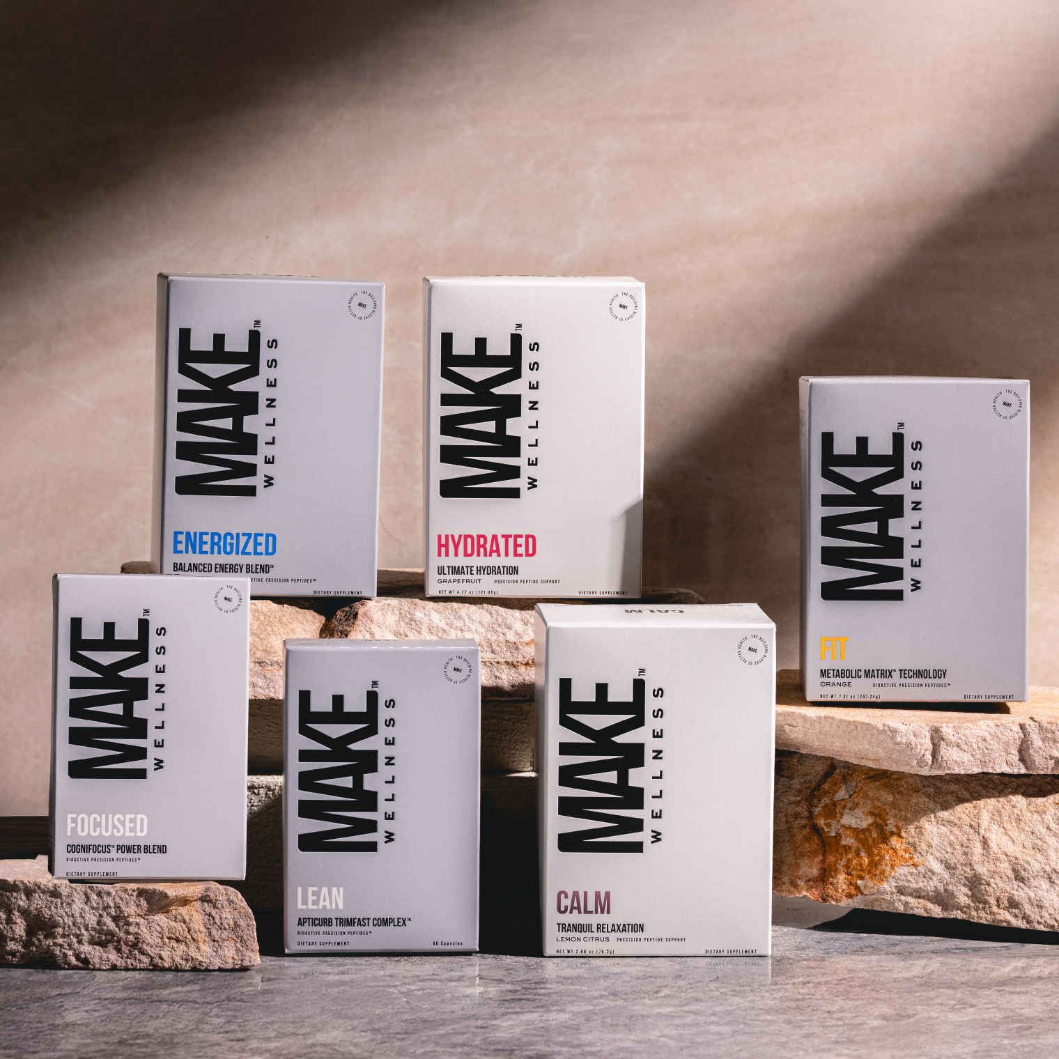 Display of MAKE Wellness supplement boxes labeled Energized, Hydrated, and Fit arranged on stone blocks